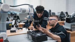 Student engineer Assembling Robotic Arm with computer in Technology Workshop. Service Engineer Holding Robot Controller and Checking Robotic Arm Welding Hardware.